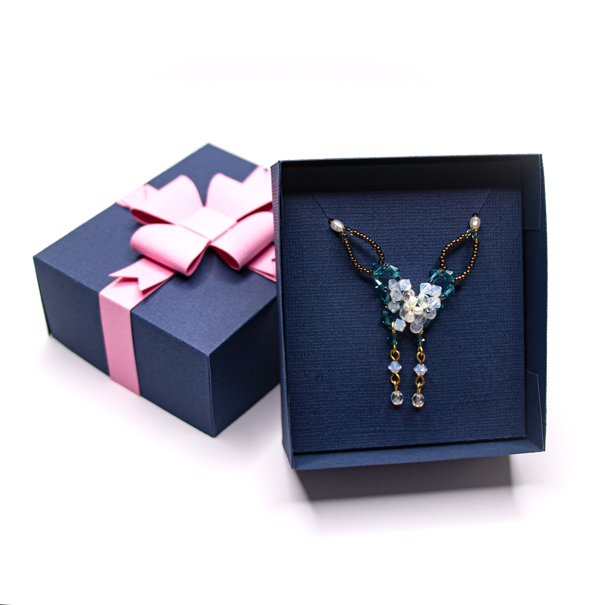Navy textured cardstock 3D necklace gift box with a Pink paper ribbon and layered bow, shown closed and with the lid lifted to reveal a beaded crystal necklace displayed on a matching insert,a jewelry packaging cut file for Silhouette Studio