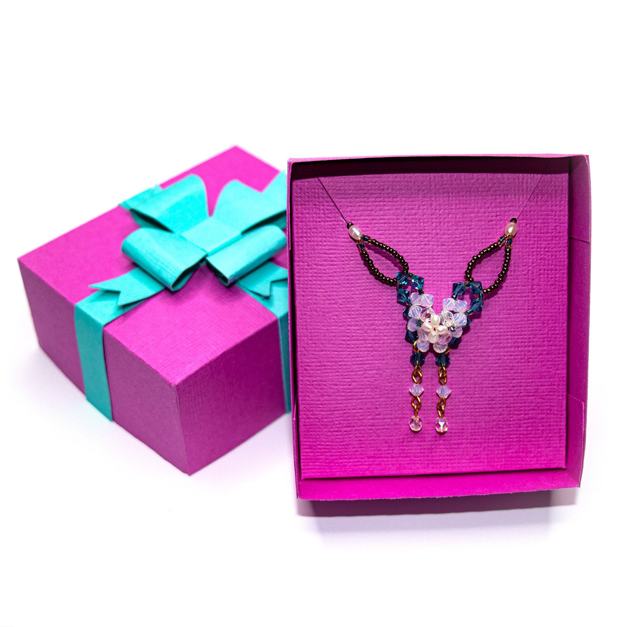 Magenta textured cardstock 3D necklace gift box with a Turquoise paper ribbon and layered bow, shown closed and with the lid lifted to reveal a beaded crystal necklace displayed on a matching insert,a jewelry packaging cut file for Silhouette Studio